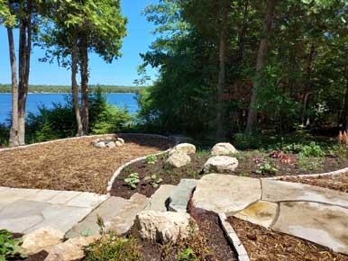 Stone walkway and landscaping next to body of water.