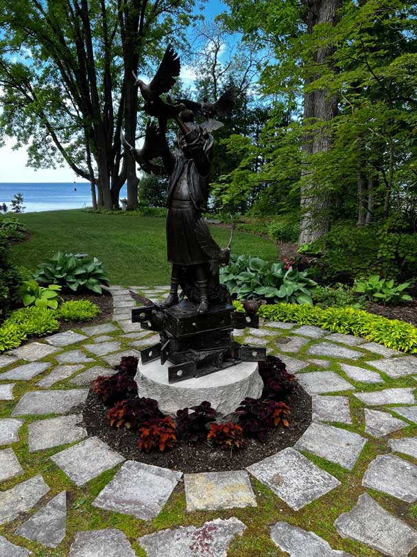 Statue surrounded by stone walkway and summer color.