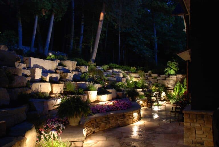 Stone wall and greenery lit up by outdoor lighting.